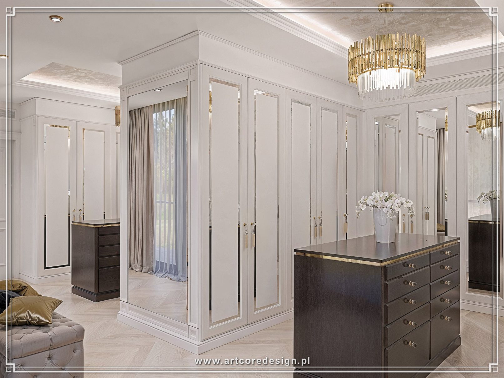 Garderoba na wymiar w domu jednorodzinnym z centralną wyspą komodową i lustrzanymi frontami szaf. Indywidualny projekt wnętrza obejmuje klasyczną zabudowę stolarską, złote uchwyty oraz dekoracyjne oświetlenie sufitowe, tworząc funkcjonalną i reprezentacyjną przestrzeń zaprojektowaną przez pracownię projektowania wnętrz.